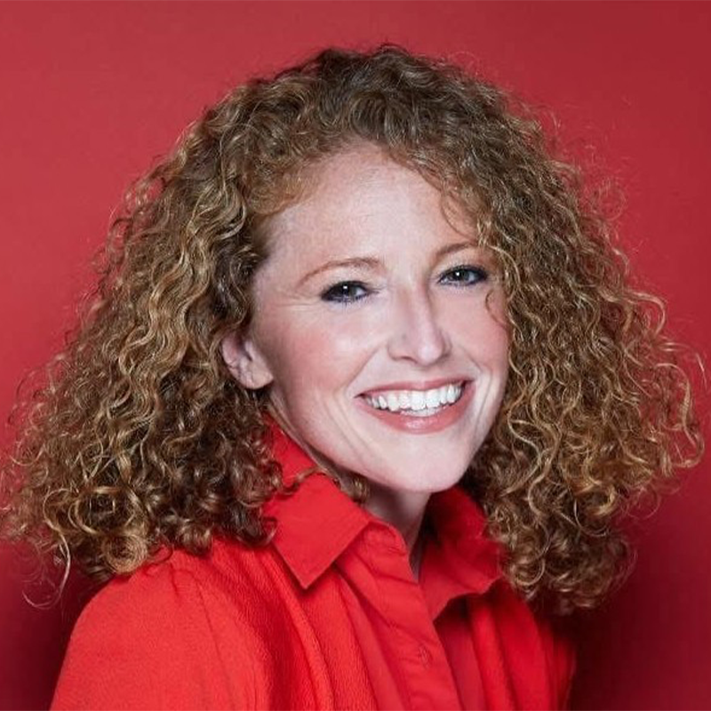 Smiling woman with fair skin and curly, light brown hair, wearing a bright red collared shirt and jacket. Marissa Mulder is posed in front of a solid red background, looking directly at the camera.