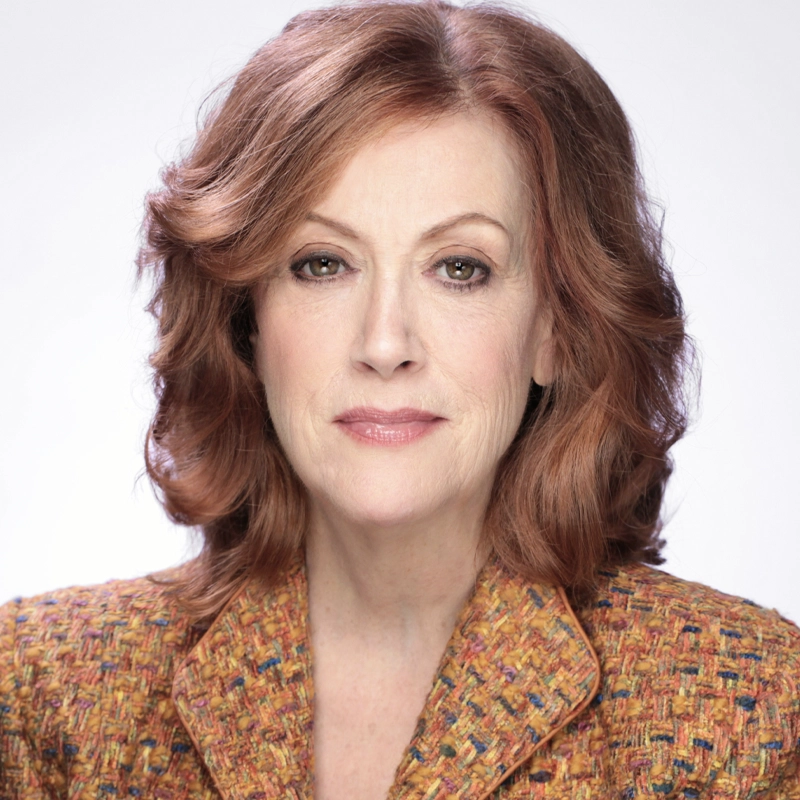Karen Murphy, a middle-aged woman with wavy, shoulder-length auburn hair, poses against a plain light background. She wears a multicolored textured blazer and has a calm, confident expression with subtle makeup and light pink lipstick.