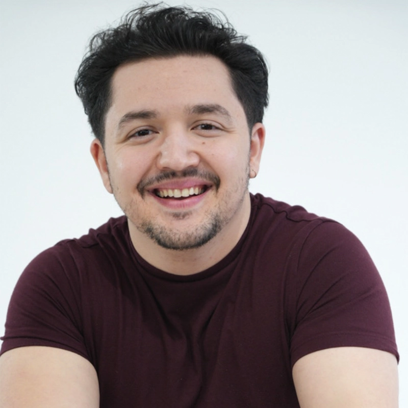Ron Galluccio, a man with short, dark hair and facial hair, smiles at the camera. He is wearing a maroon t-shirt and sits against a plain white background, his arms casually resting in front of him for a friendly, approachable vibe.