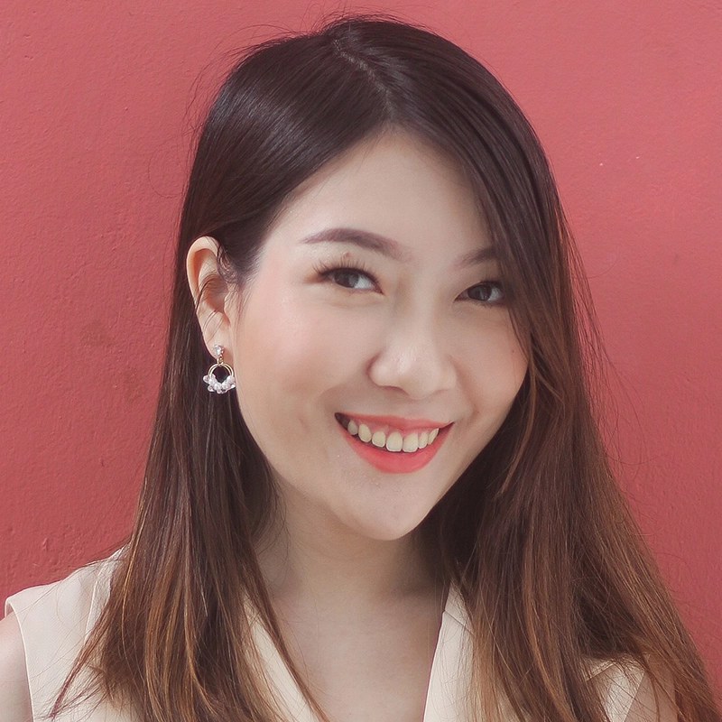 Ella Sodam Yoon, a young woman with straight, dark brown hair and fair skin, smiles warmly at the camera. She wears circular earrings and a sleeveless beige top against a plain, textured pink wall. Her side-parted hair frames her face beautifully.