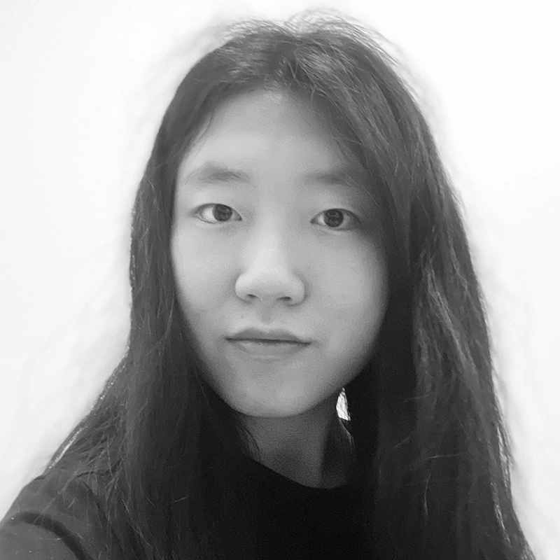 Ella Sodam Yoon, a young person with long, straight dark hair and a neutral expression, looks into the camera. The black-and-white photo features a plain, light-colored background and shows them in a dark shirt.