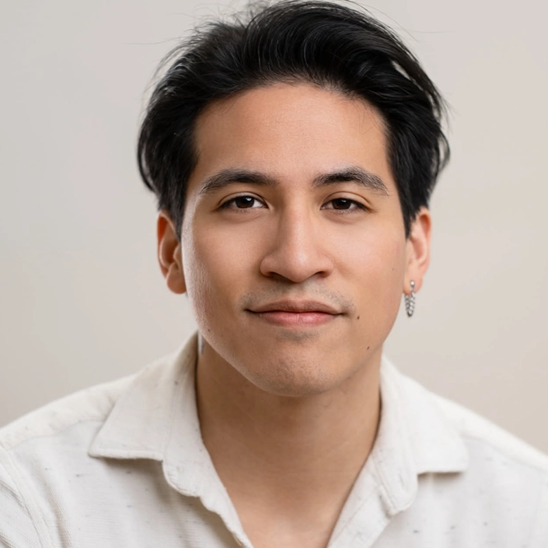 A young man with medium skin tone, black hair styled back, and wearing a white collared shirt looks directly at the camera. Joshua Carandang has a slight smile and wears a silver hoop earring in his left ear; the background is softly blurred and neutral.