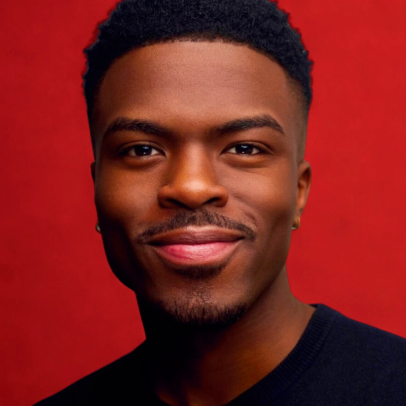 A young man with short, curly black hair and a trimmed goatee smiles softly. He wears a small earring and a dark shirt. The vibrant red background and lighting highlight his features in the style of an Allison Calabrese portrait.
