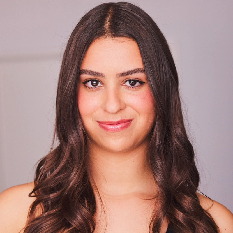 Abigail Callahan, a young woman with long, wavy brown hair and fair skin, smiles softly at the camera. She has brown eyes, subtle makeup, and is wearing a sleeveless black top against a neutral, softly lit background.