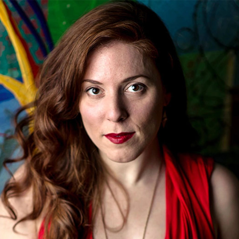 A portrait by Danny Weller of a woman with long, wavy auburn hair, fair skin, and bold red lipstick. She faces forward with a neutral expression, wearing a red sleeveless top against a colorful, abstract background.