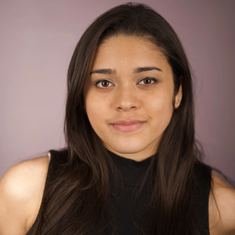 Savannah LaSalle, a young woman with long dark hair and brown eyes, looks at the camera with a slight smile. She wears a sleeveless black top and is posed against a muted purple background with soft lighting.