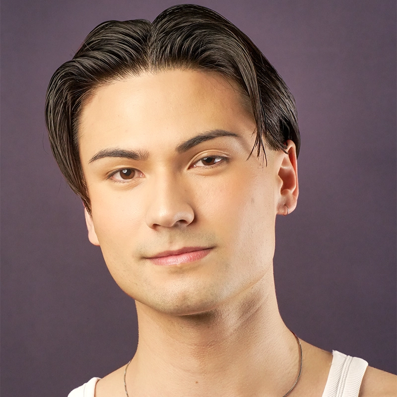 A young person with fair skin and straight, dark brown hair parted in the middle. They have groomed eyebrows, subtle makeup, and wear a white tank top and a thin necklace. The plain dark purple background creates a calm mood for this Brandon J. Large portrait.