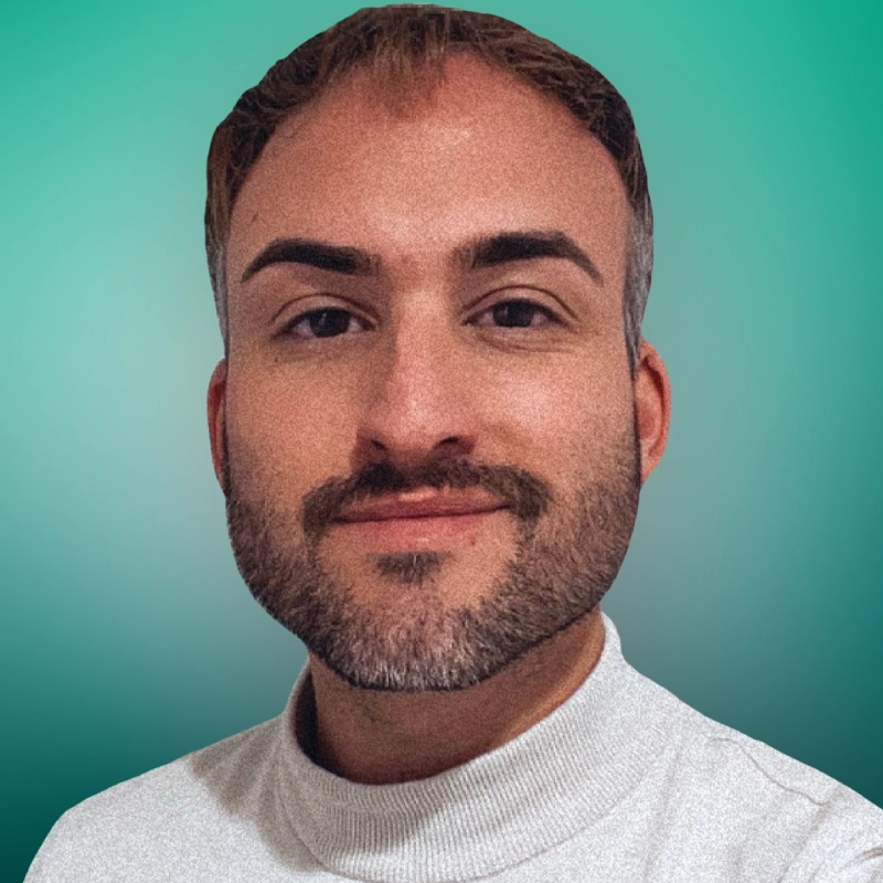 Gregg Aponte Jr., a person with short brown hair, neatly groomed beard, and dark eyebrows, is smiling slightly. They are wearing a light-colored turtleneck shirt against a smooth gradient of teal and green shades.
