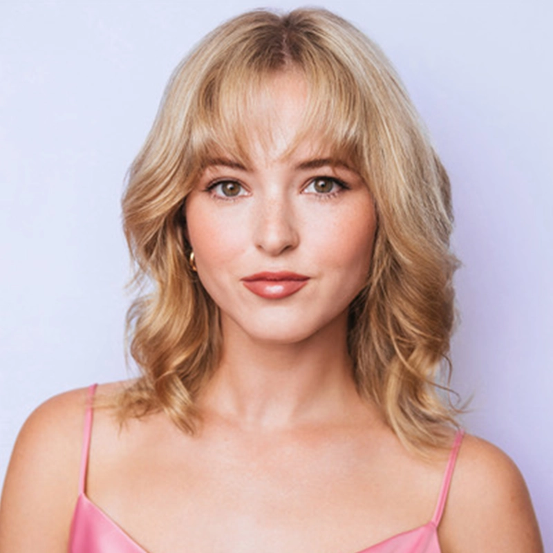 A young woman with wavy blonde hair and bangs, Caroline Portner, wears a pink spaghetti strap top. She has light skin, subtle makeup, and gold hoop earrings. She is facing forward and smiling slightly, against a pale lavender background.