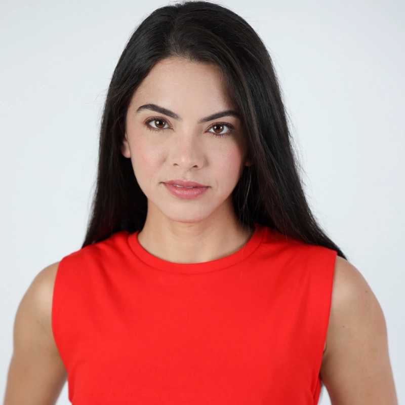 Stephanie Goulart, a woman with long straight dark hair, light skin, and brown eyes, looks at the camera with a neutral expression. She is wearing a sleeveless bright red top and stands against a plain, light-colored background.