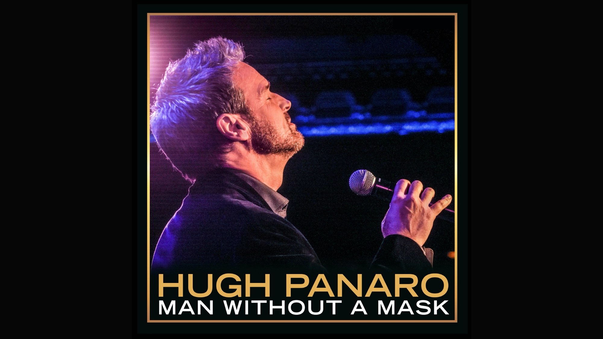 A man with short gray hair and a beard sings passionately into a microphone on stage. He wears a dark jacket and faces upward, bathed in purple-blue light. The text reads: “Hugh Panaro, Man Without A Mask.”.
