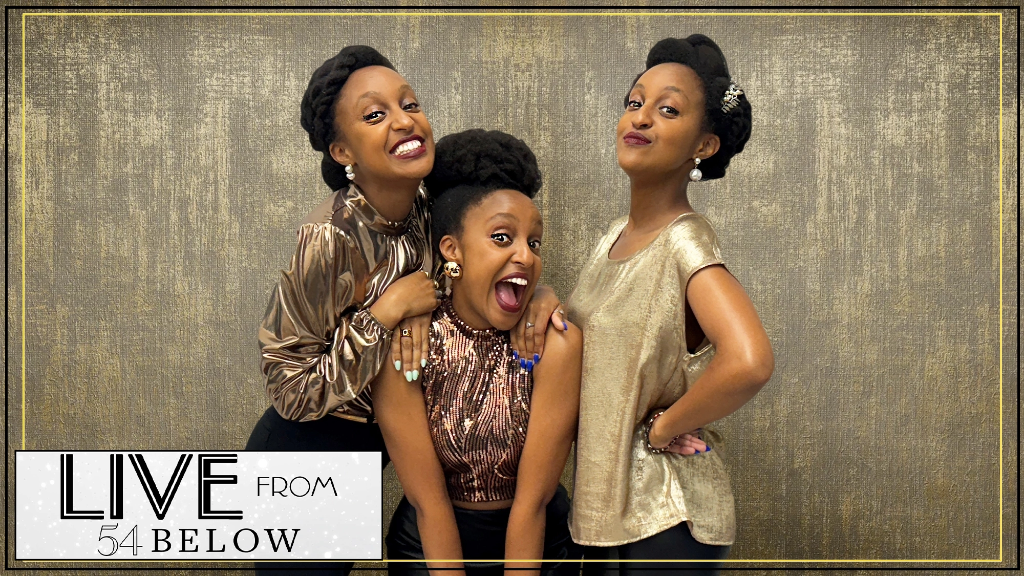 Three women with similar natural hairstyles pose together, smiling joyfully against a gold textured backdrop. They wear shiny metallic tops in gold and bronze. In the corner, a sign reads “LIVE FROM 54 BELOW”—catch the MOIPEI LIVESTREAM from NYC!.