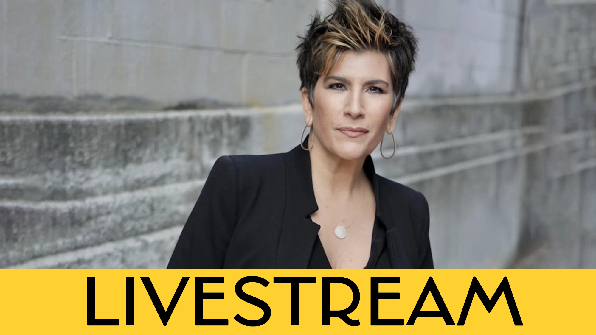 A confident person with short, styled dark hair and hoop earrings stands outdoors against a gray concrete wall, wearing a black blazer and necklace. A bold yellow banner at the bottom announces 