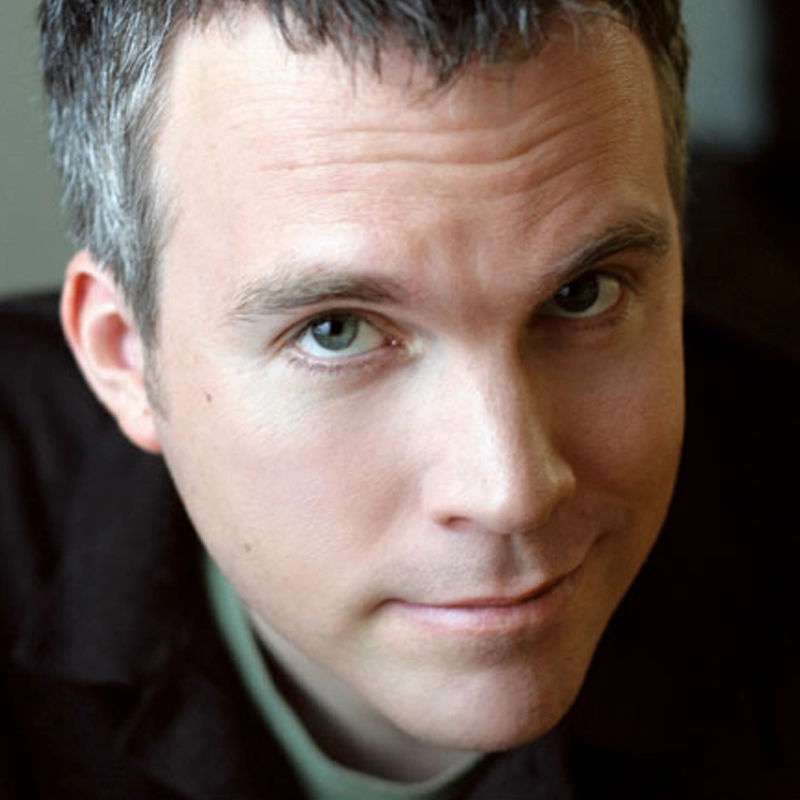 Jeff Scherer, a man with short, dark hair and fair skin, looks into the camera with a slight smile. He wears a dark jacket over a light shirt, while the blurred background keeps the focus on his face.