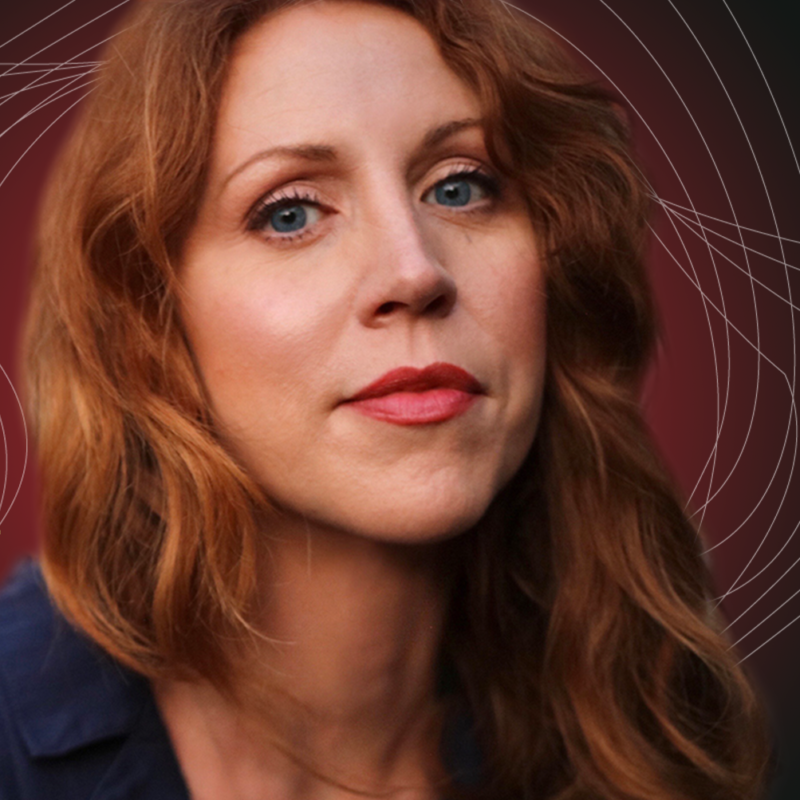 A woman with long, wavy reddish-brown hair and blue eyes looks at the camera. She wears subtle makeup with red lipstick and a dark blue top. The background is maroon with soft, abstract white line patterns.