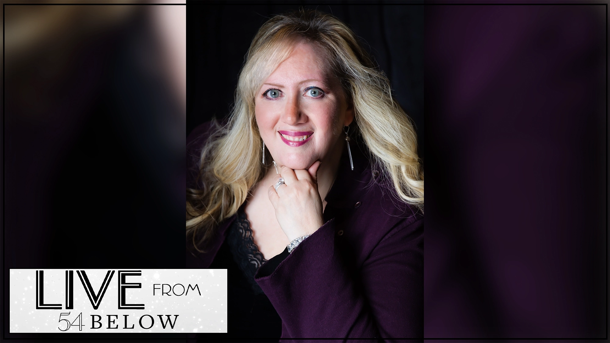 A woman with long blonde hair and light skin wears a dark purple blazer, smiling with her hand under her chin against a black background. Text in the bottom left reads 