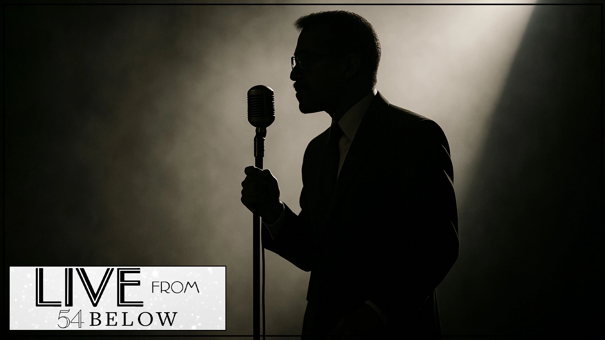 A person in a suit stands in profile, holding a vintage microphone, silhouetted against a smoky, spotlighted background. The lower left corner displays a 