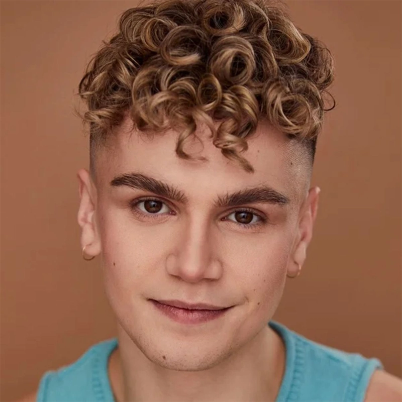 A young person with light skin and curly blonde hair looks at the camera and smiles slightly. They wear a blue sleeveless top and small hoop earrings. The warm brown background highlights the relaxed, confident vibe of Marty Lauter.