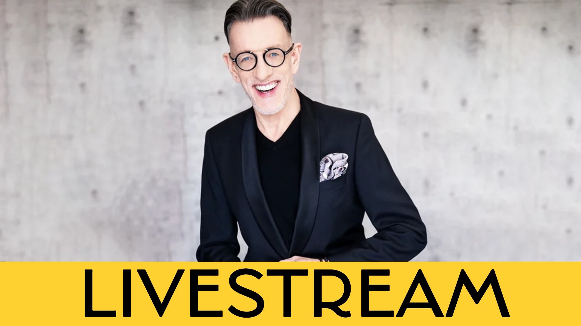 A man with glasses and short, slicked-back hair, wearing a black suit and pocket square, smiles warmly against a light gray, textured background. Large yellow text at the bottom reads “LIVESTREAM: Phillip Officer—You Fascinate Me So.”.