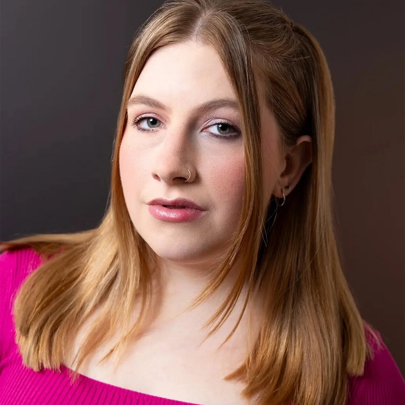 Maelyn Isenberg, a young woman with fair skin and straight, light brown hair, wears a hot pink top. She has a subtle smile, light makeup, and a silver nose ring. Her hair is parted in the middle and tucked behind her ears.