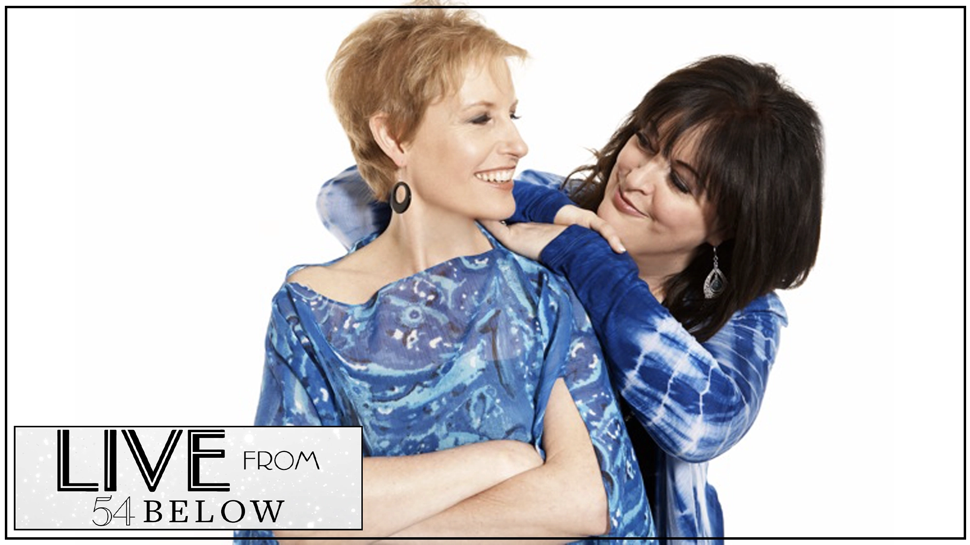LIVE Liz Callaway & Ann Hampton Callaway Two women stand closely against a white background, smiling warmly. Liz Callaway crosses her arms as Ann Hampton Callaway gently drapes her arms on her shoulders. Both wear blue patterned outfits.