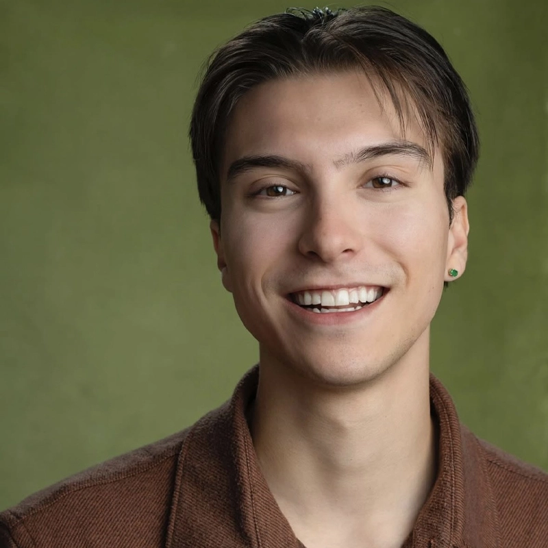 A young person with straight brown hair, fair skin, and a small earring in their left ear smiles warmly. Marco Porras wears a brown jacket over a shirt. The background is a plain, textured green with soft, even lighting.