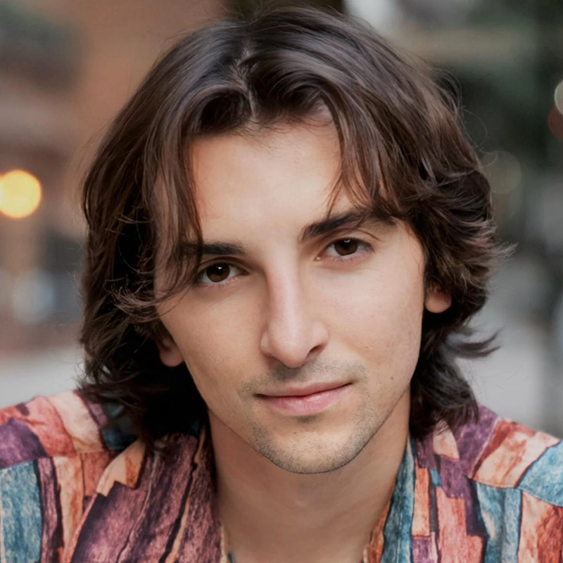 Sara Ross Avery, a young person with medium-length brown hair and light skin, is looking directly at the camera, wearing a colorful patterned shirt. The background is softly blurred, suggesting an outdoor, urban setting with warm lighting.