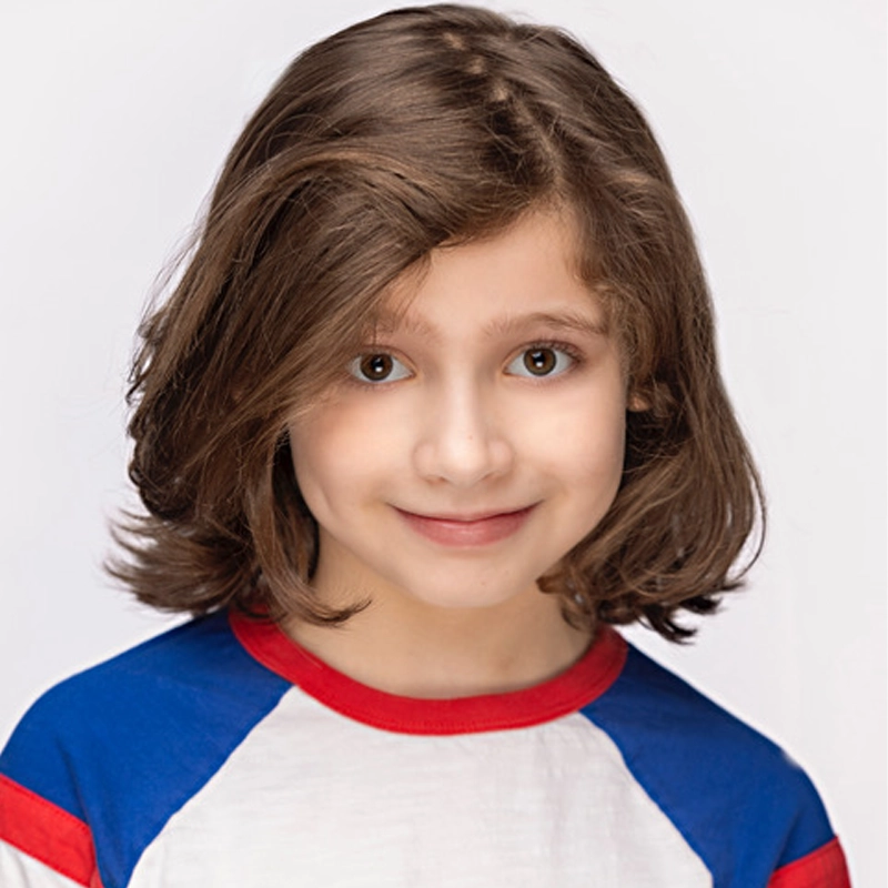 A child with shoulder-length brown hair and brown eyes smiles softly at the camera. The child wears a white shirt with blue sleeves and red trim. The background is plain white and evenly lit, focusing attention on the child’s face.