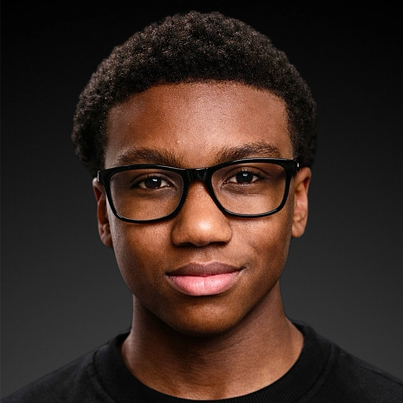 Kenneth E. Johnson Jr., a young man with short curly hair, wearing black rectangular glasses and a black shirt, faces the camera against a dark gradient background. He has a slight, confident smile and is well-lit, with even lighting highlighting his face.