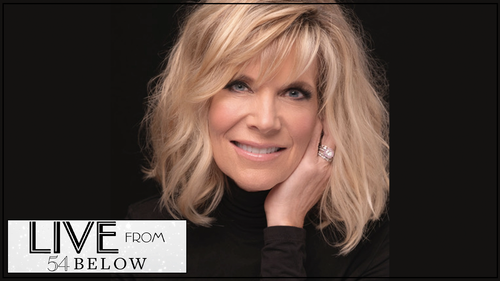 A blonde woman with shoulder-length hair and side-swept bangs smiles gently, resting her head on her hand. She wears a black turtleneck and a large ring. In the corner, a logo reads “LIVE from 54 BELOW LIVESTREAM” on a dark background—Debby Boone shines.