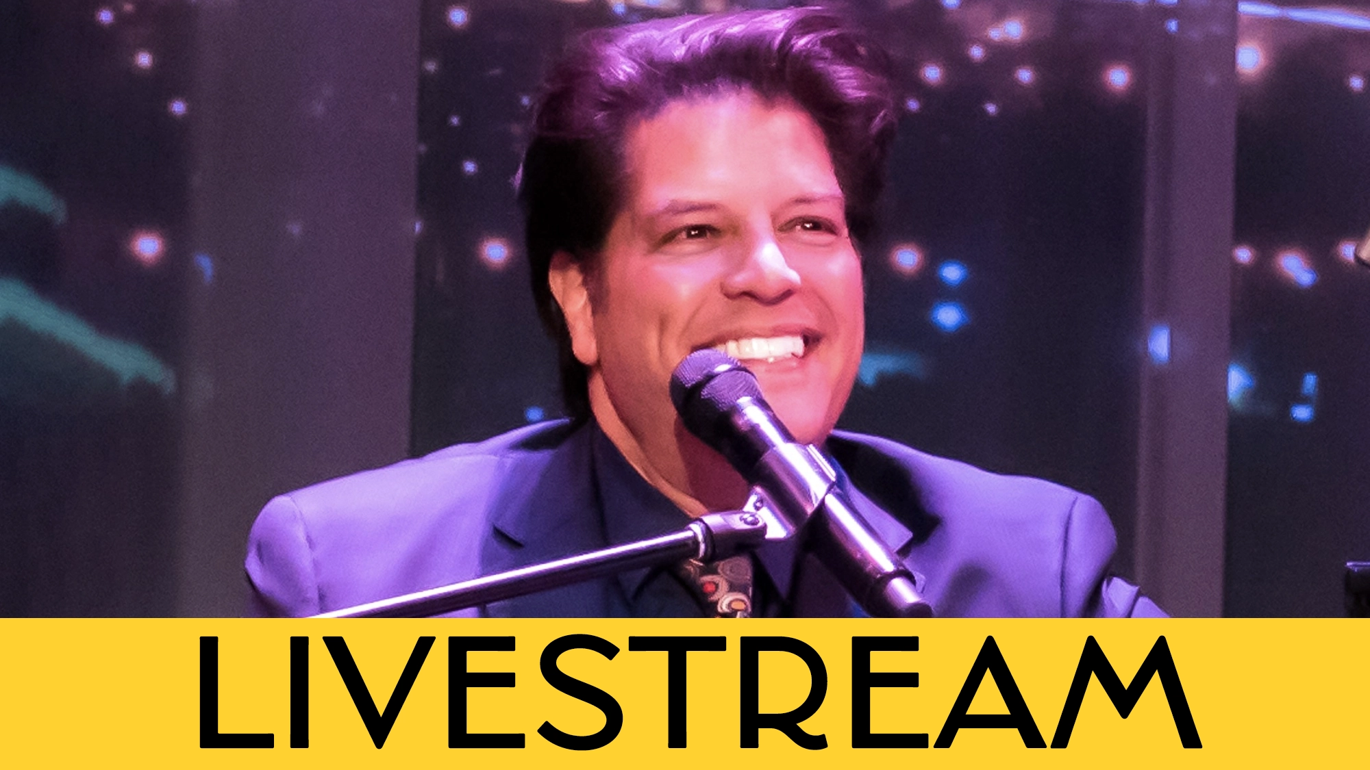 A man in a dark suit, possibly George Bugatti, smiles while singing or speaking into a microphone. Colorful lights blur in the background. A bold yellow banner at the bottom reads 