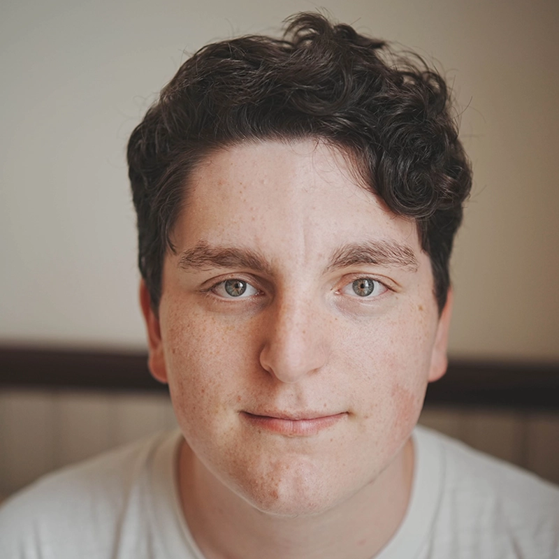 A man with curly hair and a white shirt, Micah Wolfensohn stands confidently.