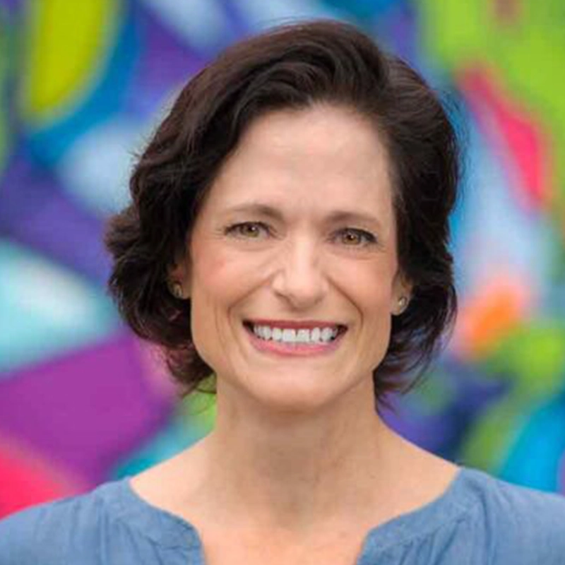 Ashley Wells smiling with shoulder-length dark hair, centered in the frame against a blurred, colorful abstract background.