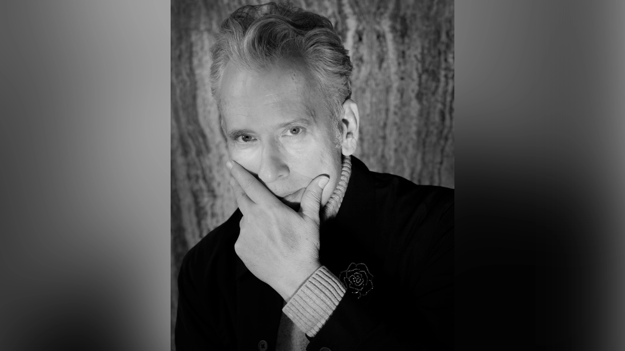 Billy Stritch - Site Image A black-and-white portrait of Billy Stritch with light hair, styled back. He gazes thoughtfully at the camera, resting his chin on his hand—celebrating 100 years of Tony Bennett. The softly textured background is gently blurred.