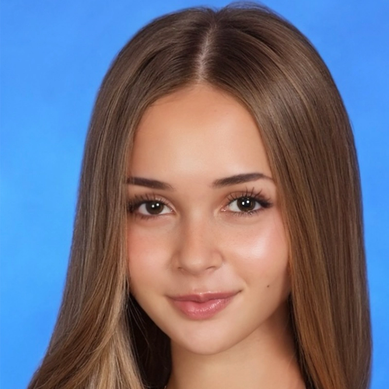 A young woman with straight, long brown hair and brown eyes smiles softly at the camera. She has clear skin, natural makeup, and wears no visible jewelry against a solid blue background.