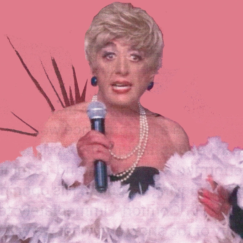A person with short blonde hair, blue earrings, and a pearl necklace holds a microphone. They wear a strapless dress and are draped in white feathers, standing in front of a solid pink background with brown abstract shapes.