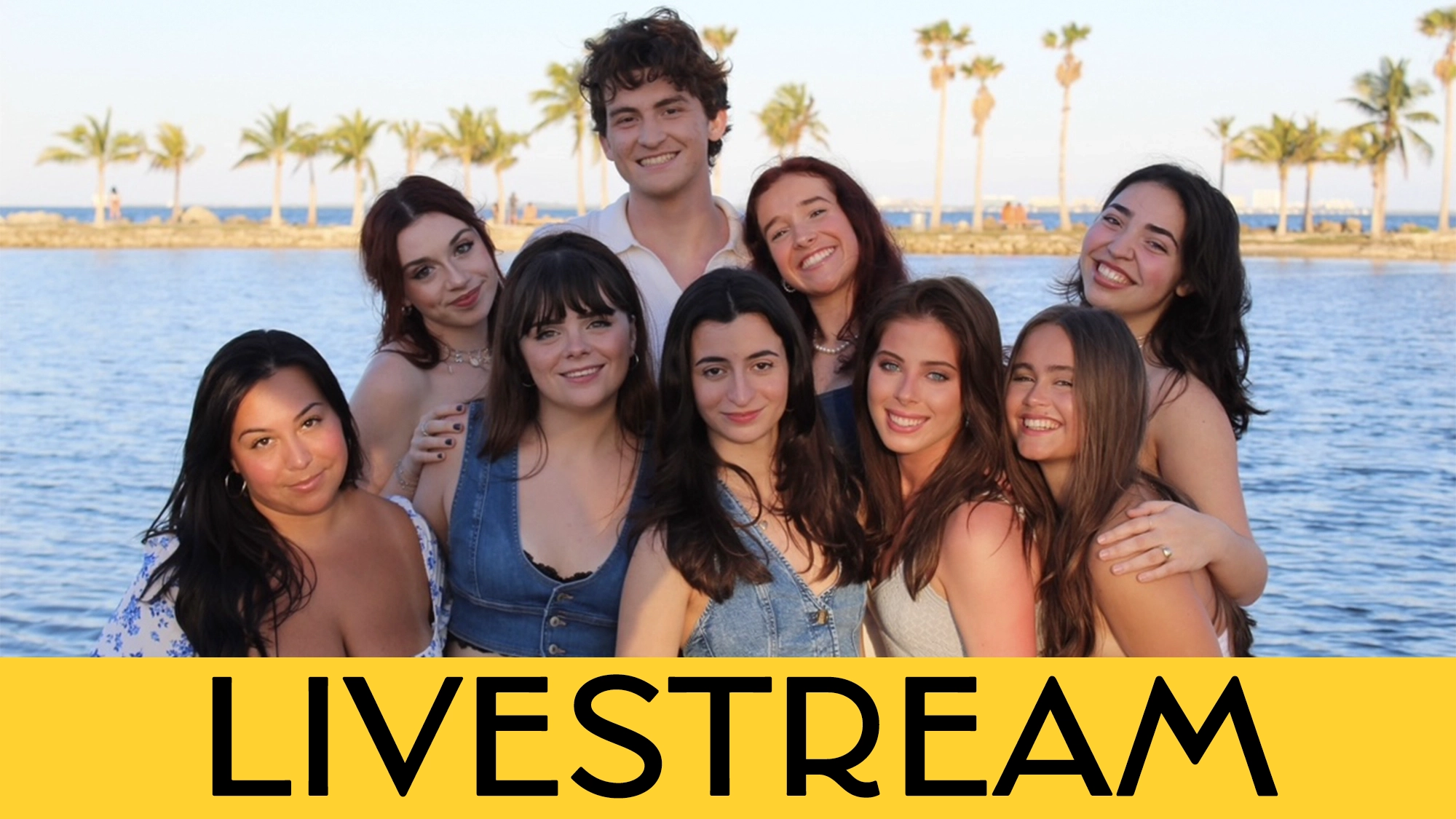 A group of ten smiling young adults, students from the University of Miami’s BFA in Musical Theatre, pose by calm water and palm trees at sunset. Six stand in back, four kneel in front. Bold yellow bar reads “LIVESTREAM” in large black letters.