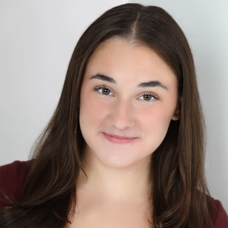 Sophia Leverett, a young woman with long, straight brown hair and fair skin, smiles gently at the camera. She has brown eyes, natural makeup, and wears a burgundy top against a plain, light-colored background that draws focus to her face.