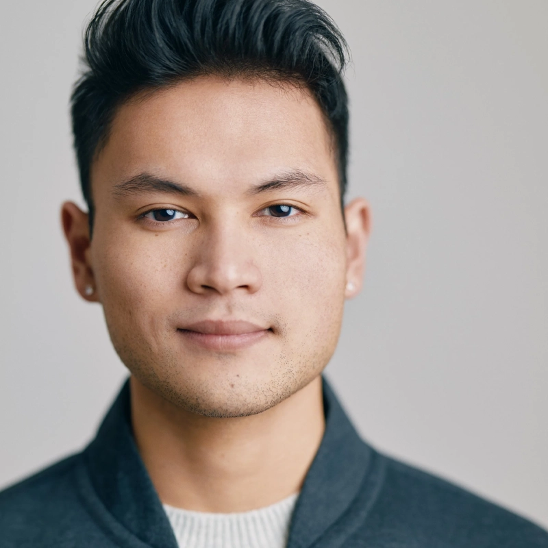 A young man, Steven Huynh, with short, dark hair and light facial hair looks directly at the camera with a neutral expression. He is wearing a dark gray jacket over a light sweater, against a plain, light-colored background that keeps the focus on his face.