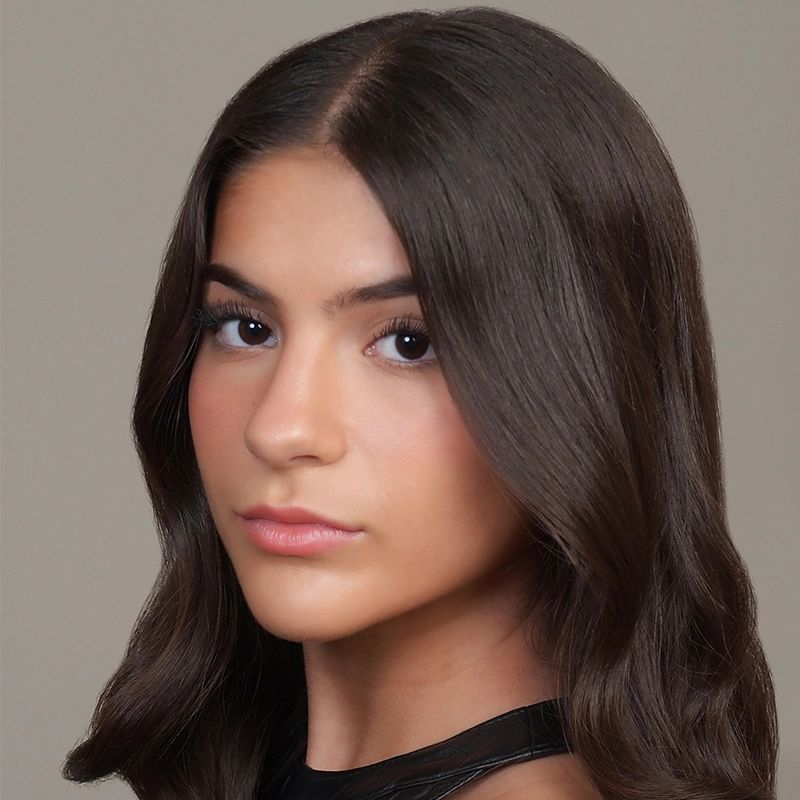 A young woman, Sophia Leverett, with long, dark brown hair parted in the middle and styled in soft waves. She has smooth, tan skin, full eyebrows, and natural makeup. She wears a black top and looks directly at the camera against a simple light background.