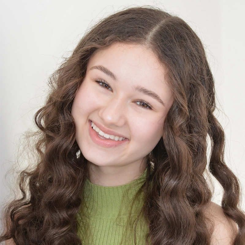 Sophia Leverett, a young woman with long, brown, curly hair and fair skin, smiles warmly. She wears a sleeveless, light green ribbed top and is posed against a plain, light background. Her expression is cheerful and friendly.