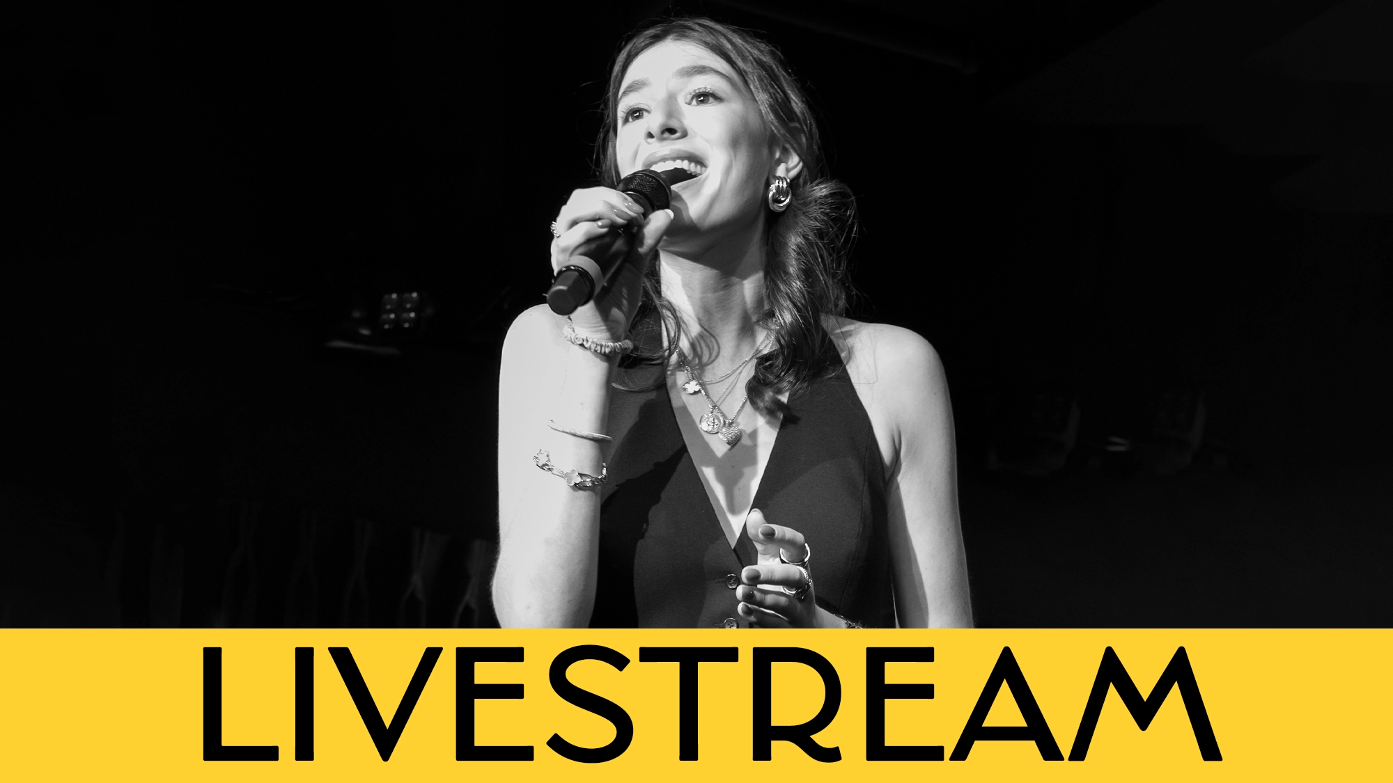 Olivia Katz calendar image A woman sings into a microphone on stage, smiling and wearing a dark sleeveless dress. The lower portion of the image features a bold yellow banner with the word