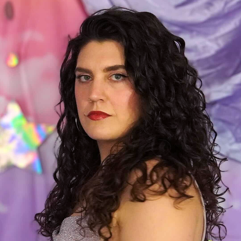 HaleyJane Rose, with long, dark, curly hair and red lipstick, gazes confidently at the camera in a sleeveless, sparkly top. The background features draped purple and pink fabric with a shiny star decoration.