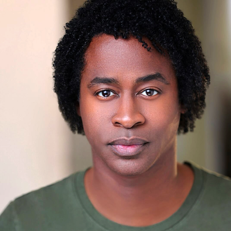 A person with short curly black hair and brown skin faces the camera, wearing a green shirt. They have a neutral facial expression, and soft lighting highlights their features—reminiscent of a portrait style popularized by Steven Cutts.