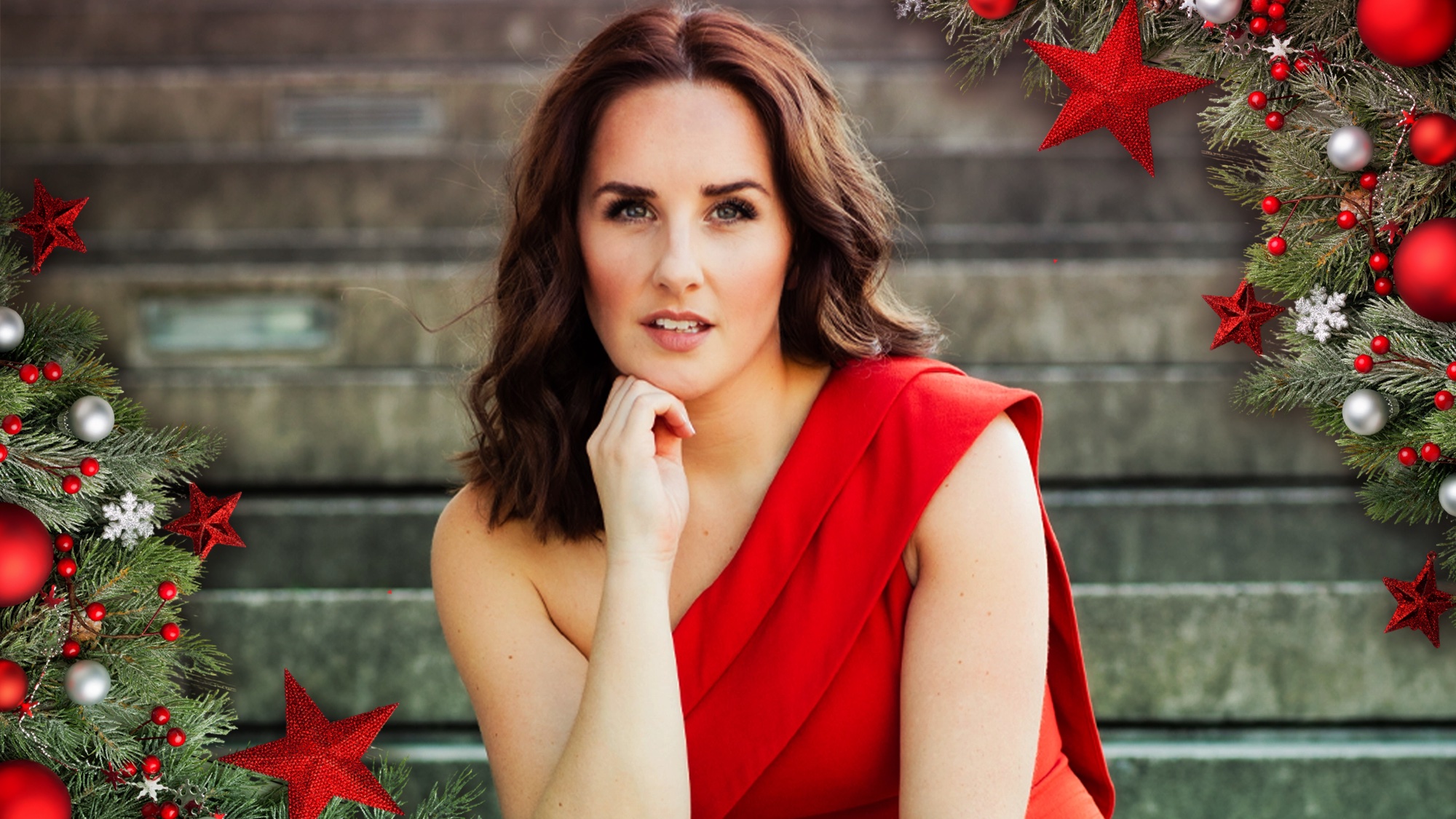 A woman with wavy brown hair in a red one-shoulder dress sits on stone steps, resting her chin on her hand. Festive Christmas decorations frame the photo, evoking the spirit of a holiday concert filled with pine branches, red ornaments, and stars.