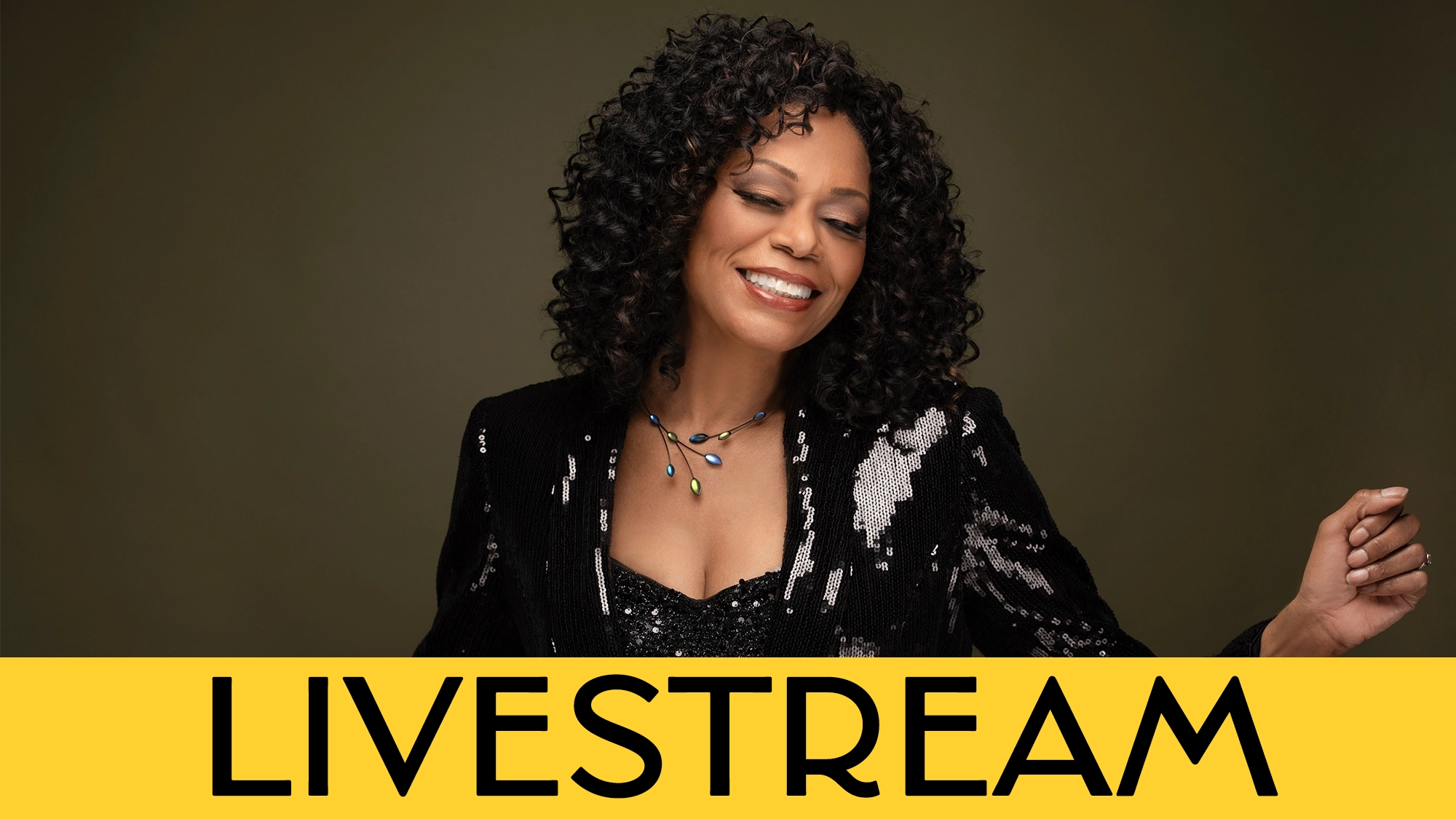 A woman with curly black hair, wearing a sparkly black jacket and jeweled necklace, smiles with her eyes closed against a dark background. A bold yellow banner at the bottom reads “LIVESTREAM: Stephanie Pope Livin’ It Up” in large black letters.