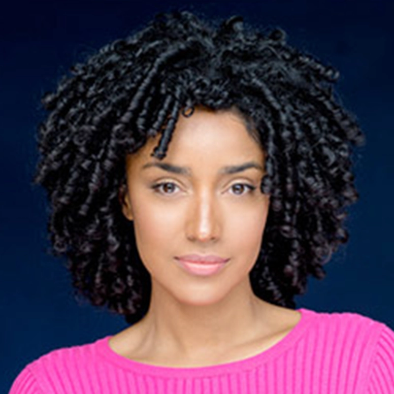 Sandra Valls, with medium-brown skin and dark, curly hair in defined ringlets, poses against a deep blue background. She wears a bright pink, ribbed top and has a calm, neutral expression with minimal makeup.