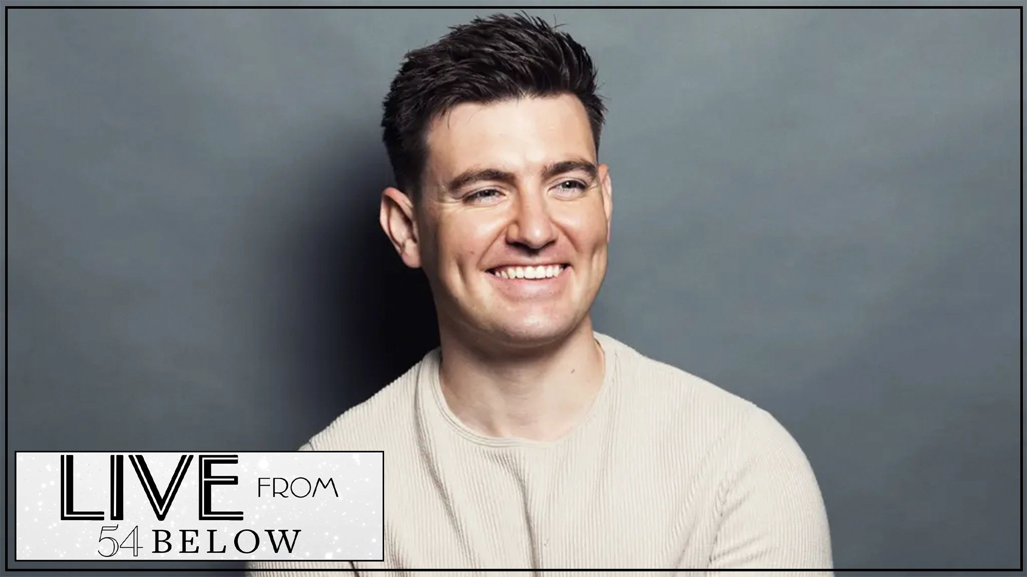 A man with short dark hair, wearing a light beige textured sweater, smiles while looking off to the side against a plain gray background. In the lower left corner, a graphic reads “LIVE FROM 54 BELOW” with modern black and gray text.
