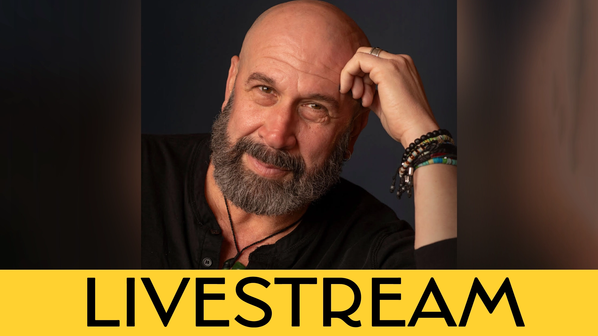 A bearded, bald man wearing beaded bracelets and a ring gazes at the camera in a black shirt. The yellow banner below reads “LIVESTREAM”—don’t miss Jeremy Schonfeld sharing his Songs of Jeremy Schonfeld live.