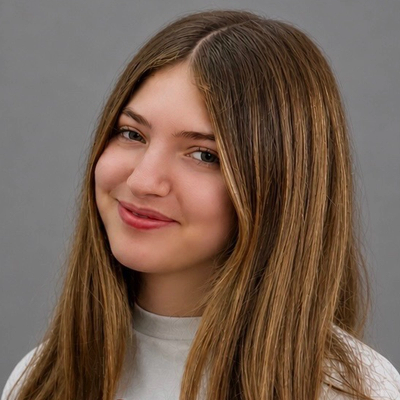 A young woman with long, straight, light brown hair smiles gently. She is wearing a light gray turtleneck shirt and looking slightly to her left. The plain gray background gives the portrait a clean, Matthew Brand studio-like appearance.